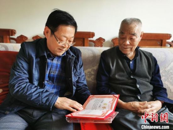 图为青海省红十字会副会长陈安民(左)与齐福魁(右)老人一边交流一边看老人获得的证书。 孙睿 摄